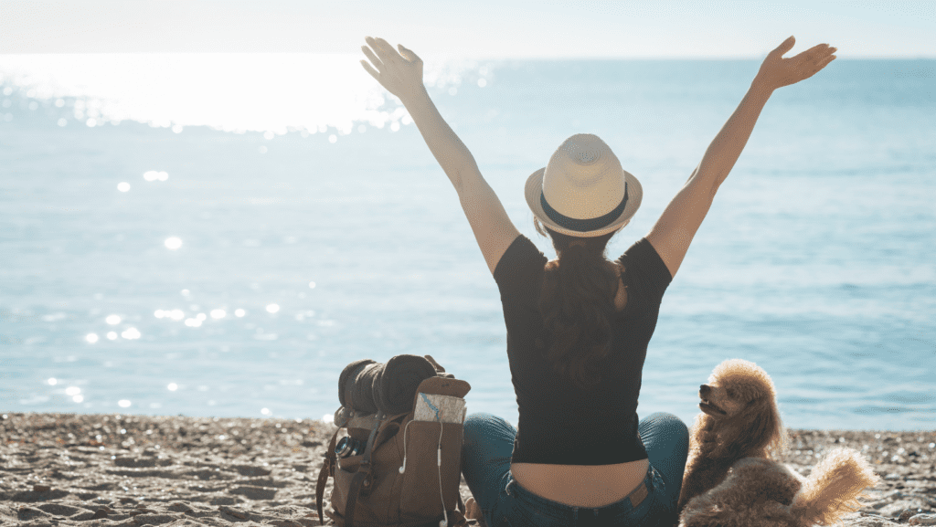 An owner with hands in the air against a beautiful view in happiness at being able to travel with her dog,