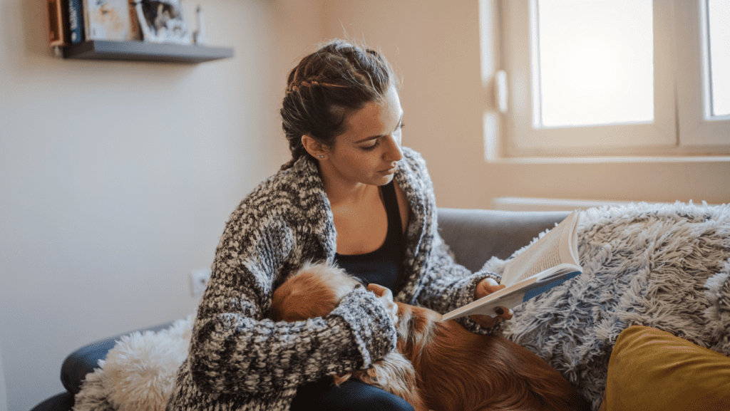 A lady going about her day, reading a book with her dog by her side.