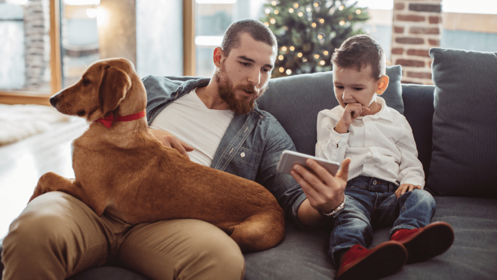 A dad and his son and his dog all spending time together on the couch.