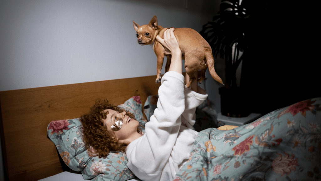 A lady in bed with an eye mask on loving her dog.