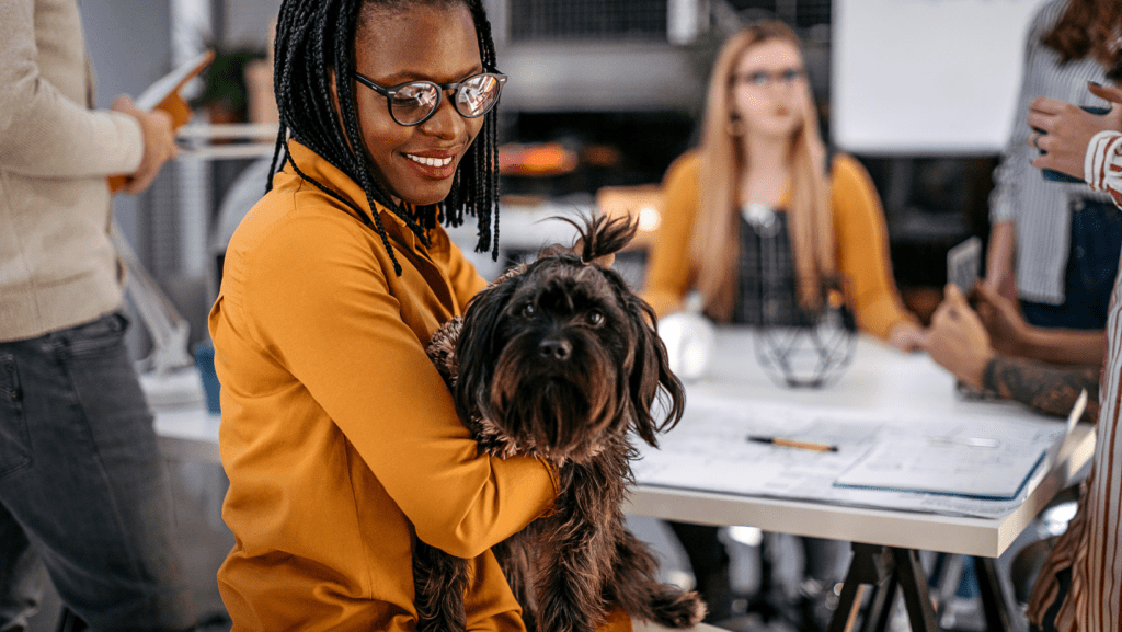Professional woman holding a small dog in a pet-friendly office, showcasing the positive impact of pets at work
